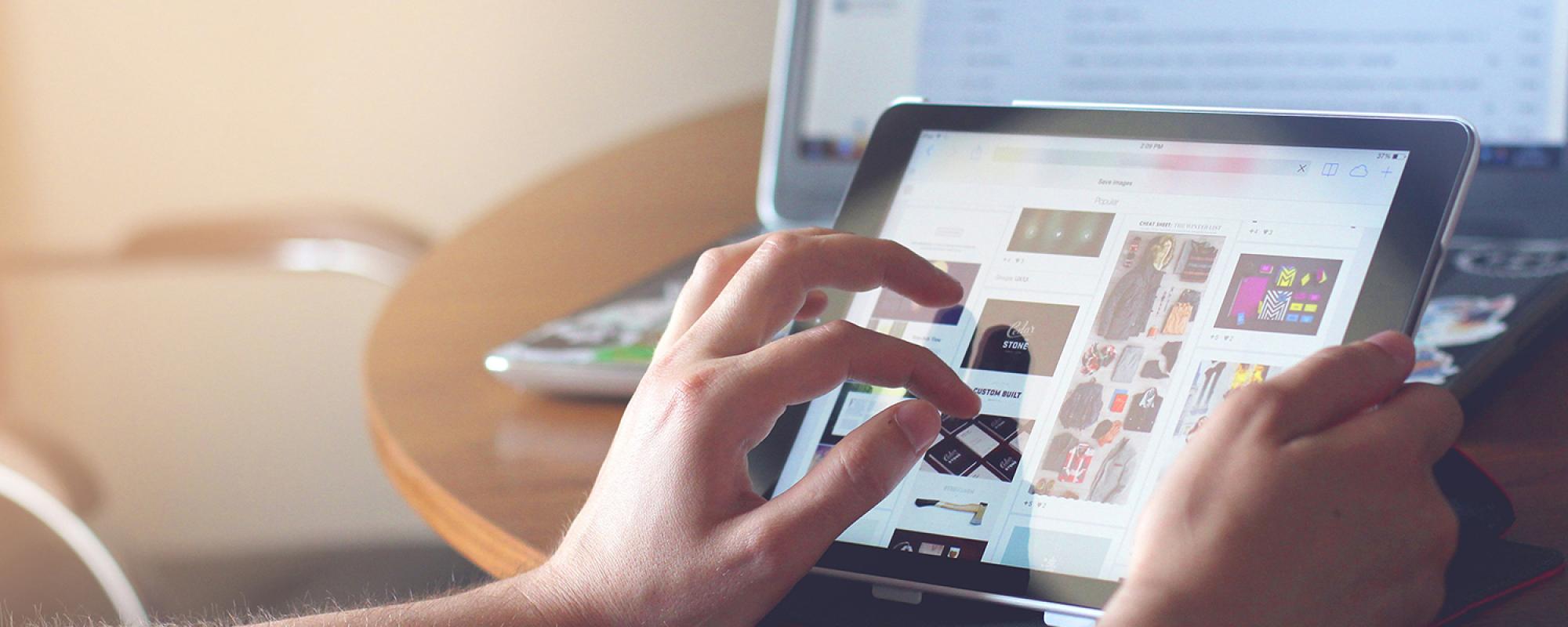 Person using tablet with information in front of a laptop screen